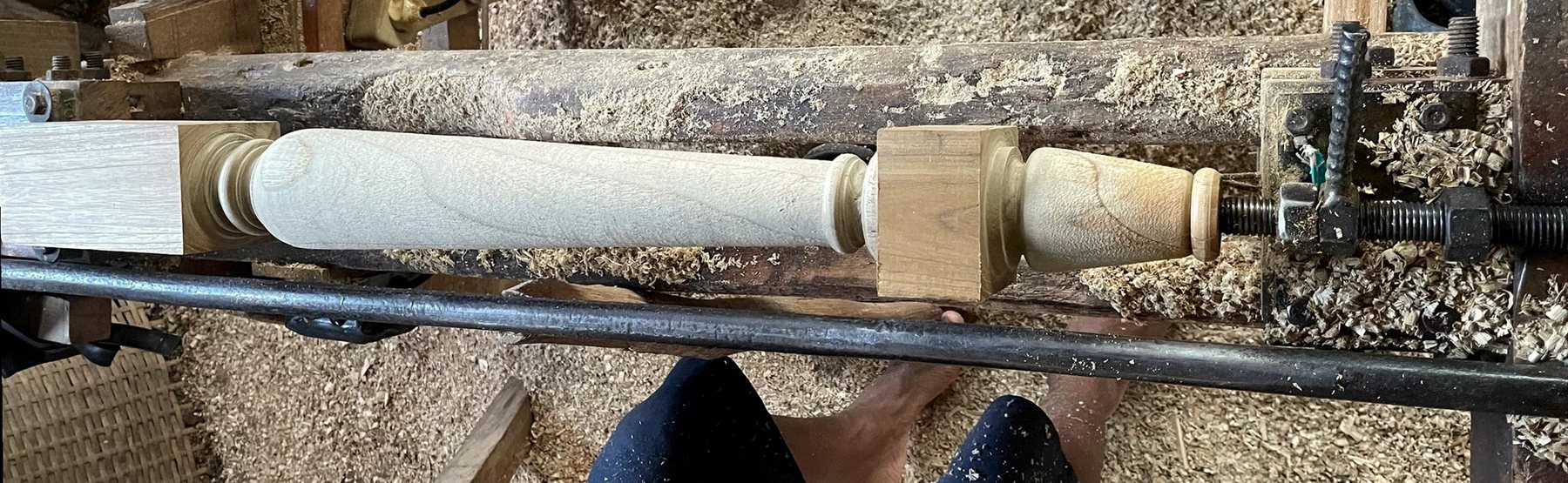 A table leg being turned on a lathe, surrounded by wood shavings